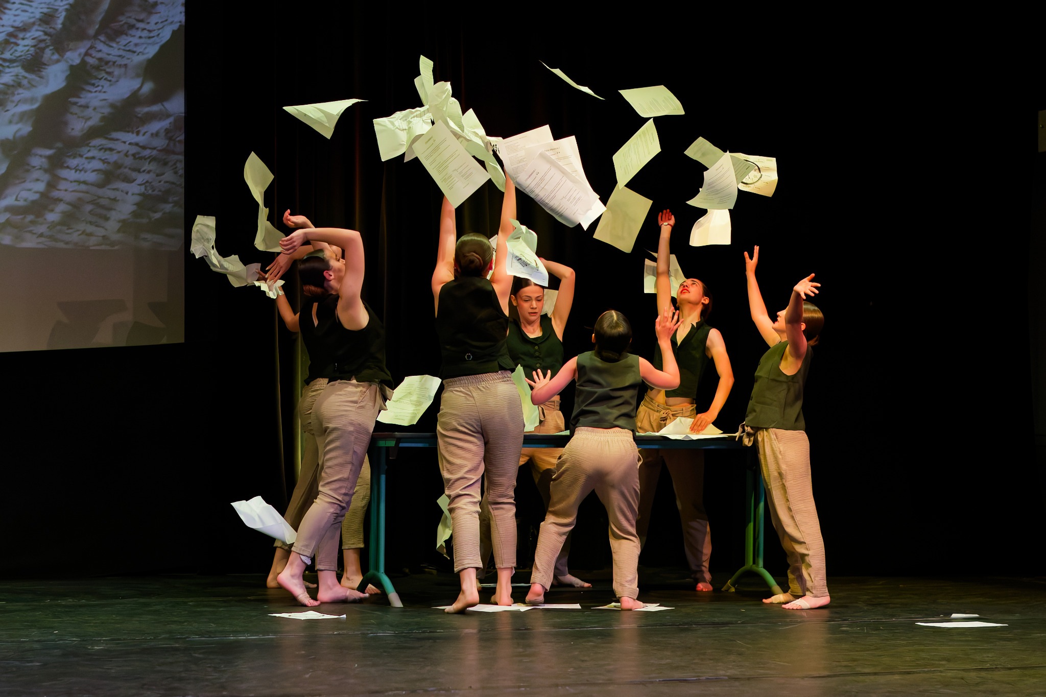 Un groupe de danseuses lance des feuilles de papier au-dessus d’une table sur scène
